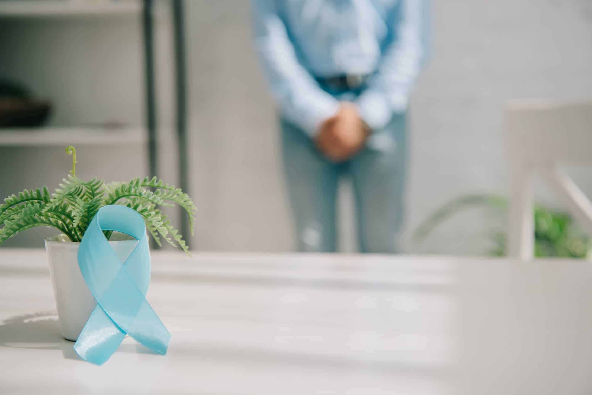 selective focus of blue awareness ribbon near flowerpot and man standing by wall and holding